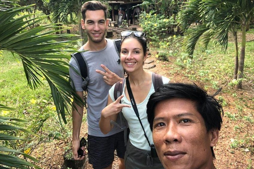 Three people in a tropical outdoor setting with greenery and palm trees. 3
