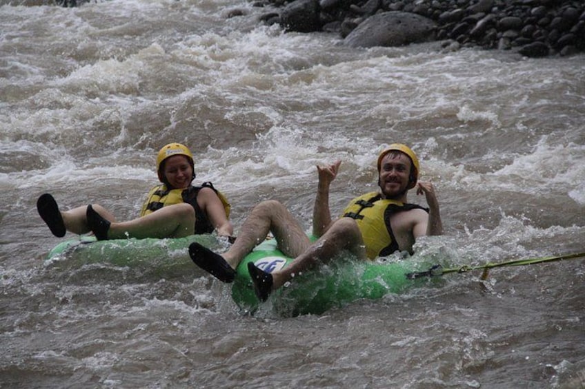 Two people on a green raft in a river with rapids. 3