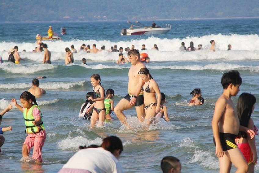 Una playa concurrida donde gente nada y juega en el agua. 4