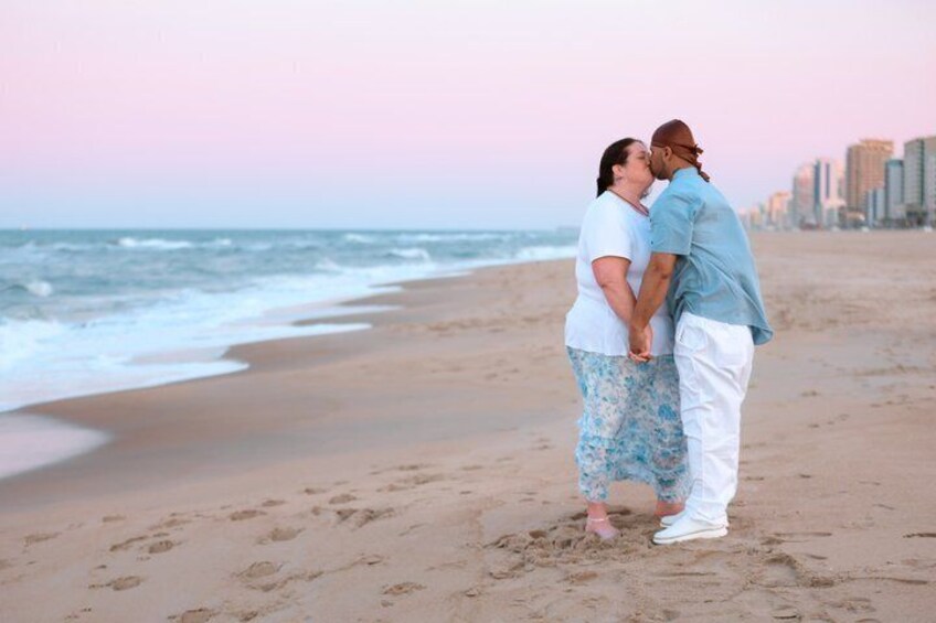A couple standing on a beach with the ocean and a city skyline in the background. 2