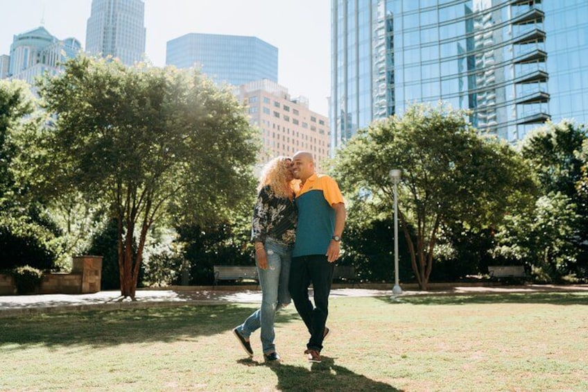 Una pareja caminando en un parque con árboles y edificios al fondo. 2