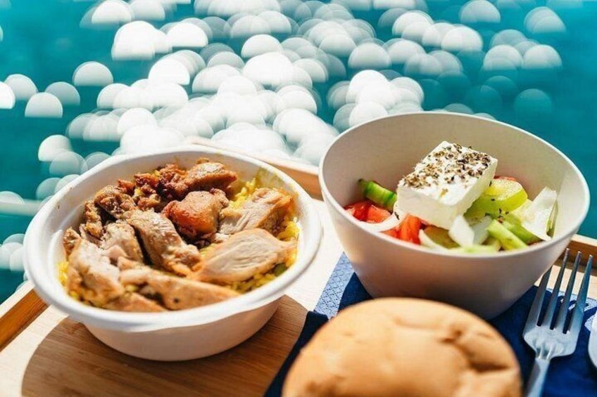 Un plato de pollo y verduras, un bol de ensalada y un panecillo sobre una mesa de madera junto a una piscina. 5