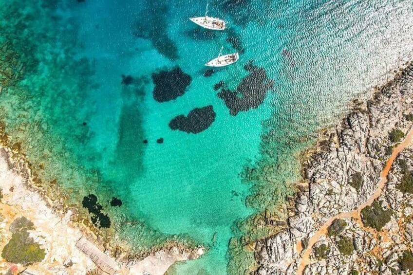 Zona costera con aguas turquesas cristalinas, costa rocosa y algunas embarcaciones. 1