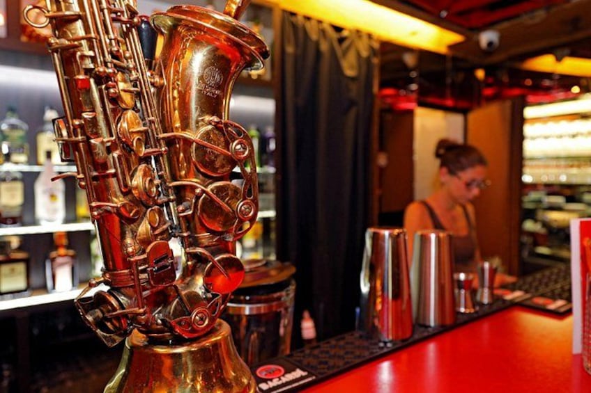 Un shaker à cocktails en forme de saxophone est posé sur le comptoir d’un bar, avec un barman en arrière-plan. 1