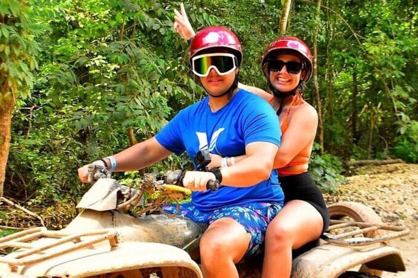 Deux personnes sur un quad dans une zone boisée. 1