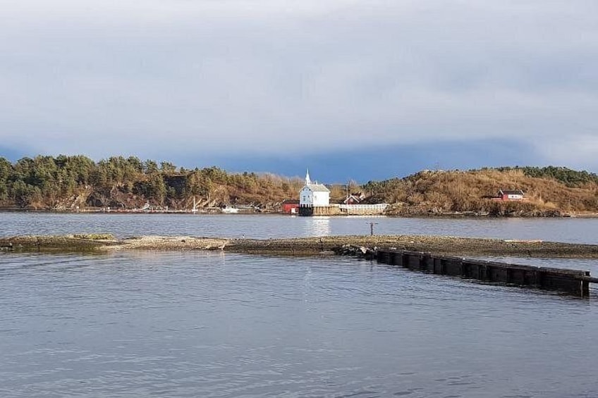 Ein ruhiger See mit einem Steg, der sich ins Wasser erstreckt, ein kleines weißes Gebäude am Ufer und ein bewaldeter Hügel im Hintergrund. 4