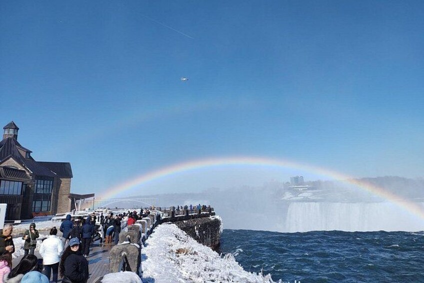 A rainbow over a frozen waterfall, a crowd of people, and a building. 2
