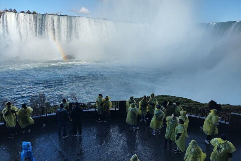 A group of people in raincoats observing a waterfall with a rainbow. 4