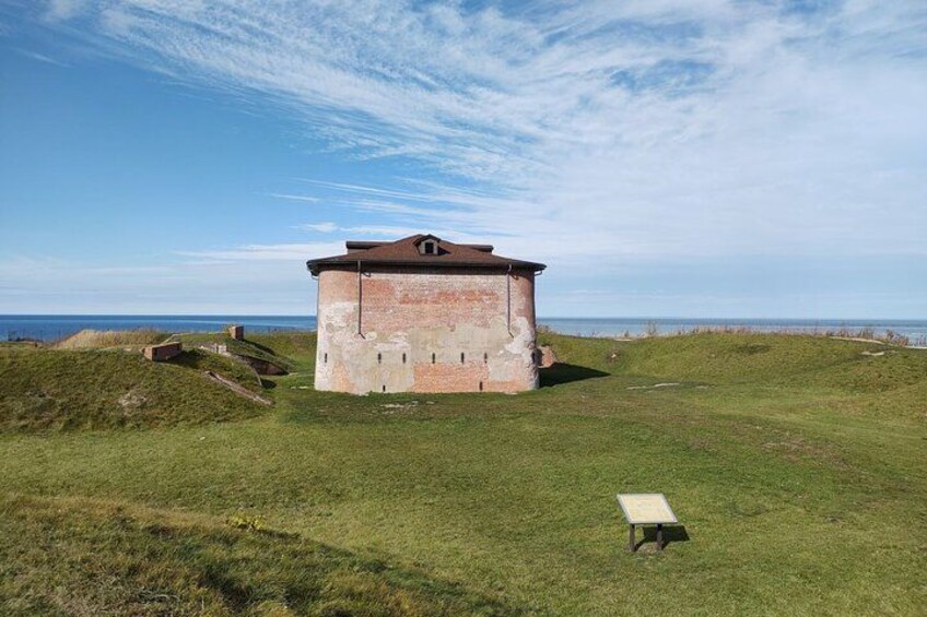 A historical brick building with a flat roof, surrounded by grassy terrain and a clear sky. 4