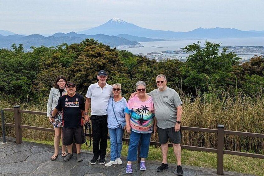Un groupe de personnes se tient sur un sentier, avec une vue sur une montagne et une étendue d’eau en arrière-plan. 2