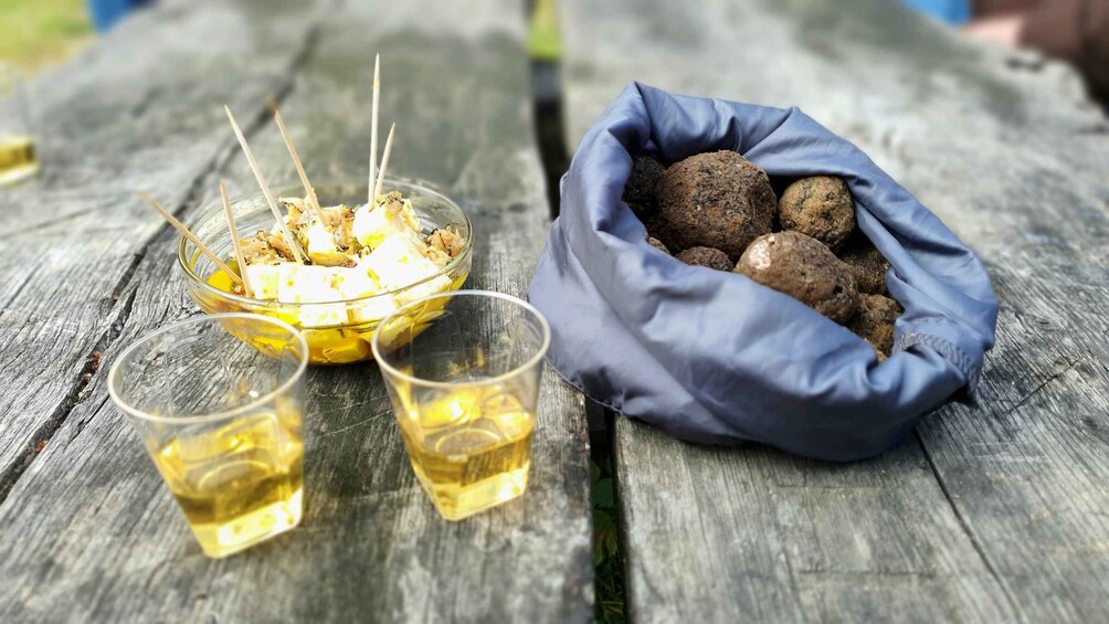 Una mesa de madera con un cuenco de queso feta, dos copas de un líquido amarillo y una bolsa de albóndigas. 2