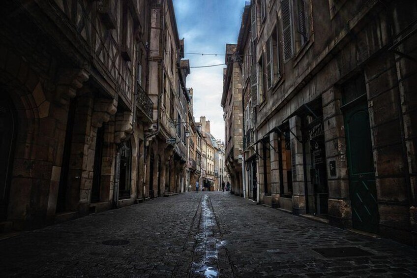 Une rue pavée bordée de bâtiments historiques aux fenêtres en arc et dont la surface est mouillée. 1