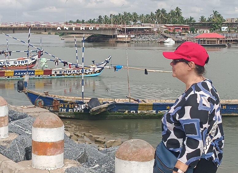 A person standing by a river with boats, a bridge, and buildings in the background. 2