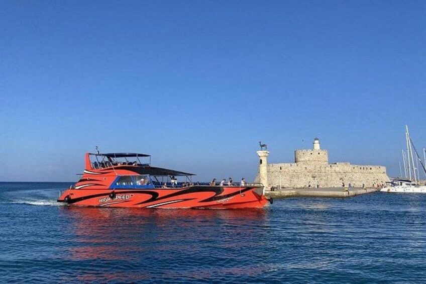 Un velero rojo llamado 'HIGH PEED' cerca de un edificio de piedra histórico con un faro. 3