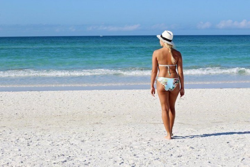 Una persona con traje de baño y sombrero caminando sobre una playa de arena, con el océano al fondo. 5
