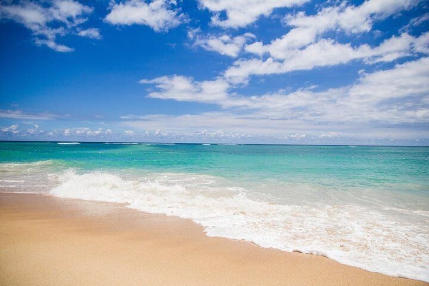 Una playa con aguas turquesas transparentes y una orilla arenosa bajo un cielo parcialmente nublado. 3