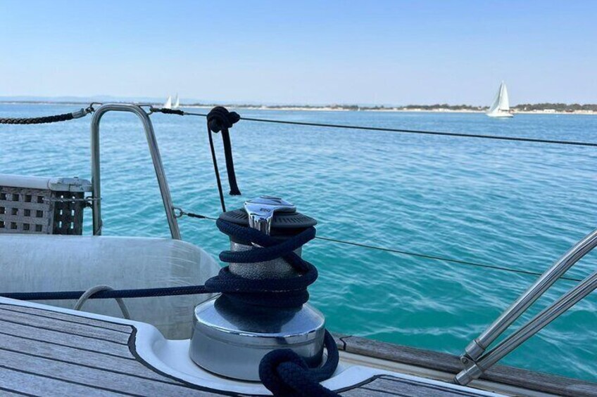 Het dek van een zeilboot, met een lieren en touwen, kalm turquoise water en een afgelegen zeilboot. 1