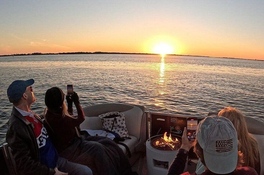 Menschen in einem Boot bei Sonnenuntergang, mit einem Feuerkorb und ruhigem Wasser. 3