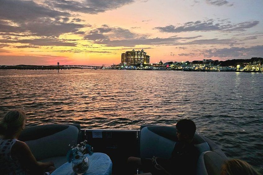 A sunset over a body of water with a pier extending into the water. There are buildings in the background, and a boat with two people on it. 2