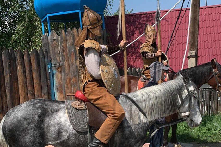 Una persona a caballo con armadura y casco medievales, y otra persona con vestimenta similar al fondo. 2