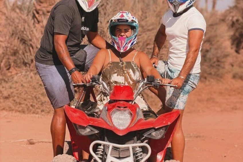 Eine Person auf einem roten Motorrad mit Helm, eine weitere Person hilft, und eine dritte Person steht daneben. 2