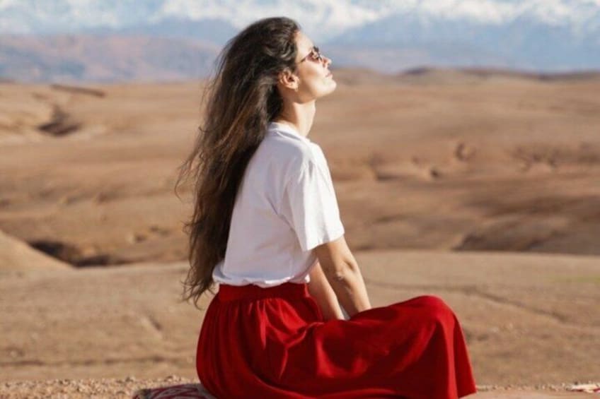 A person sitting on the ground in a desert landscape with mountains in the background. 5