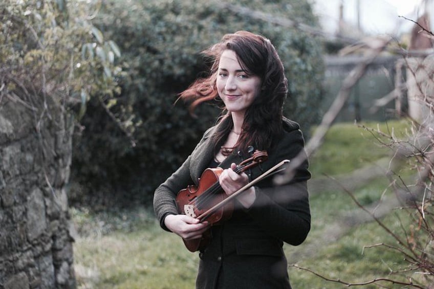 Una persona tocando el violín en un entorno natural con árboles y césped. 1