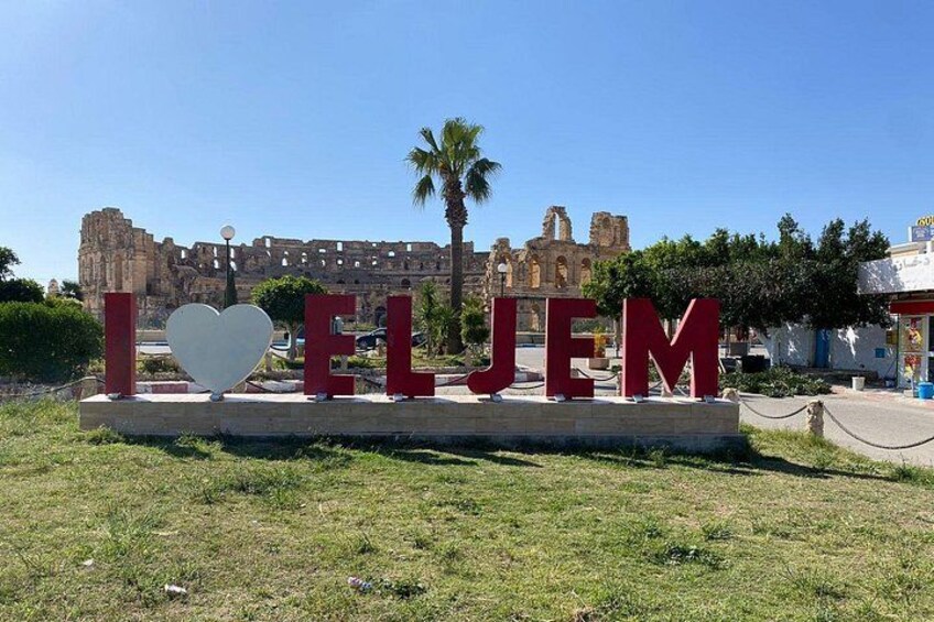A sign with the words 'I ♥ ELJEM' and a heart-shaped object in front of a historical building. 4