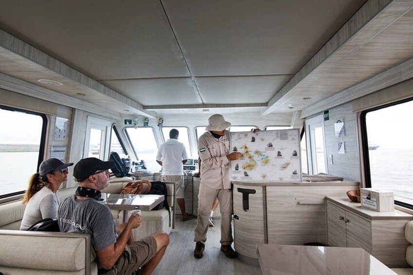 L'intérieur d'un bateau, avec un coin repas, une personne debout au poste de pilotage et une carte accrochée au mur. 3