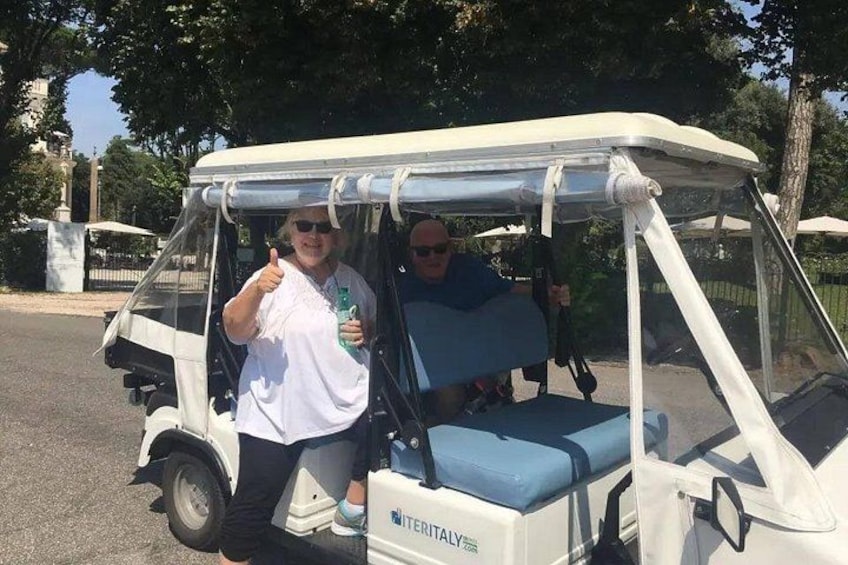 En golfbil med ett tak, en person som visar tummen upp och en annan person som håller i ett glas. 3