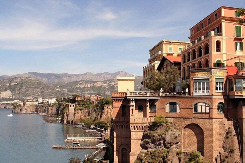 A coastal town with buildings along the cliffside, a body of water, and distant mountains. 2