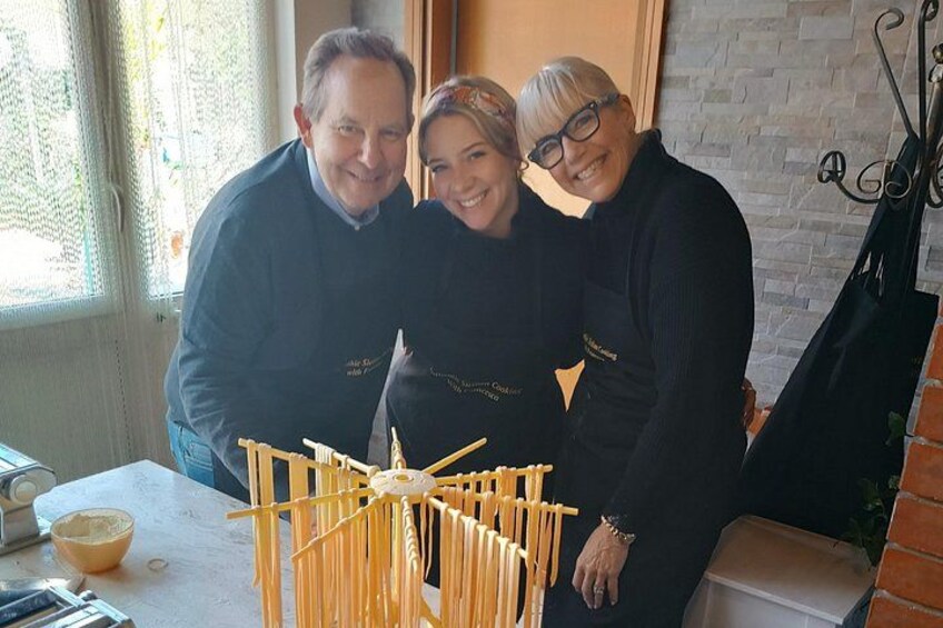 Three people standing by a table with a pasta drying rack and a bowl of sauce. 5