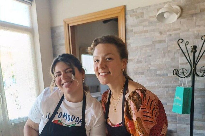 Two people wearing aprons with a kitchen setting in the background. 3