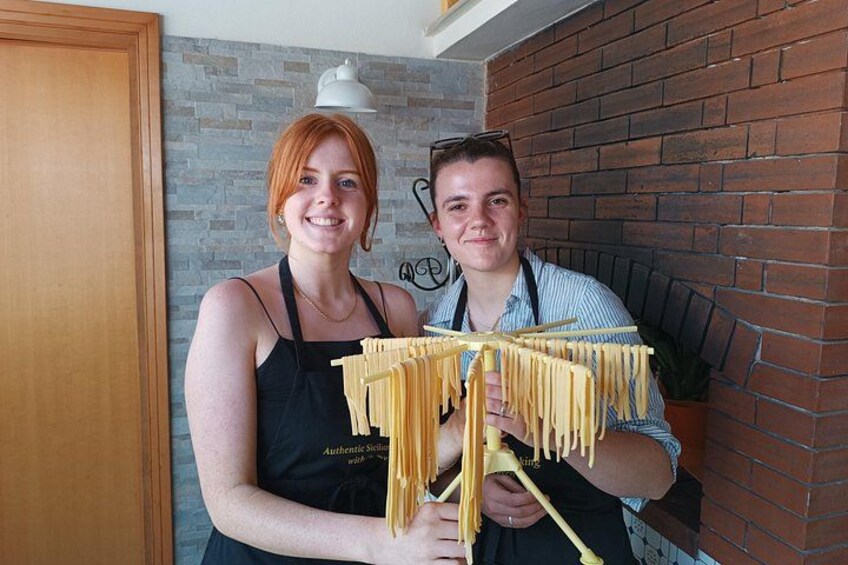 Two people holding a pasta-making machine. 1