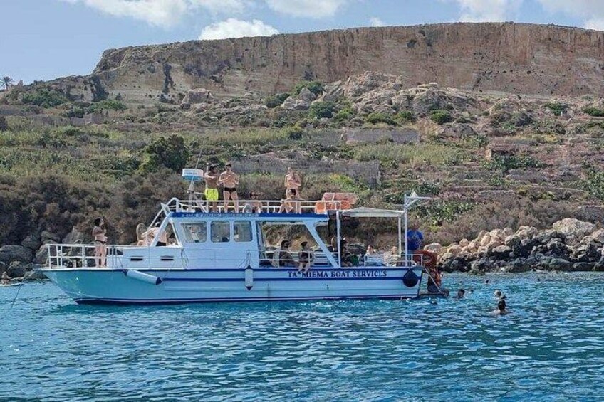 Un bateau portant le nom « PIAGETTA BOAT SERVICES » navigue sur des eaux calmes, avec une côte rocheuse et des falaises en arrière-plan. 1