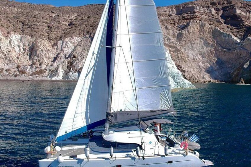 A sailboat with a white sail, a person standing at the stern, and rocky cliffs in the background. 3