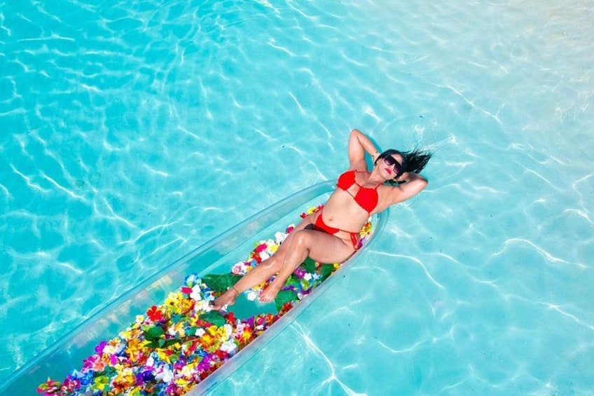 A person lying on a floating platform in a clear blue pool, surrounded by colorful flowers. 2