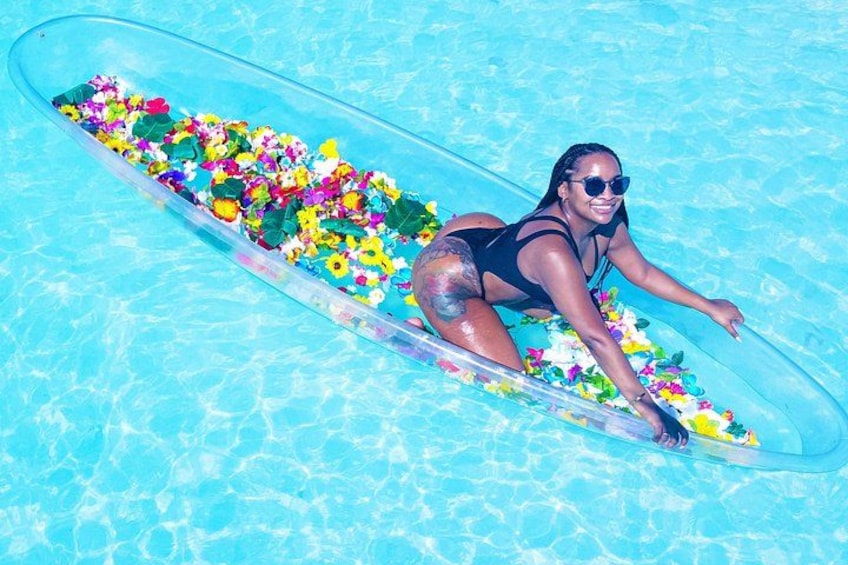A person lying on a surfboard in a pool surrounded by colorful flowers. 4