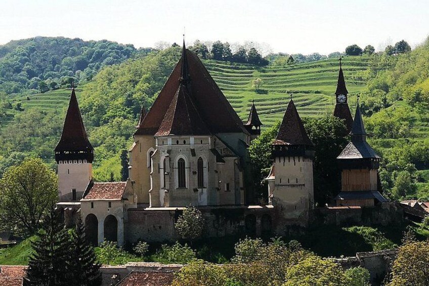 A historic castle with multiple towers and a church, surrounded by lush green hills. 3