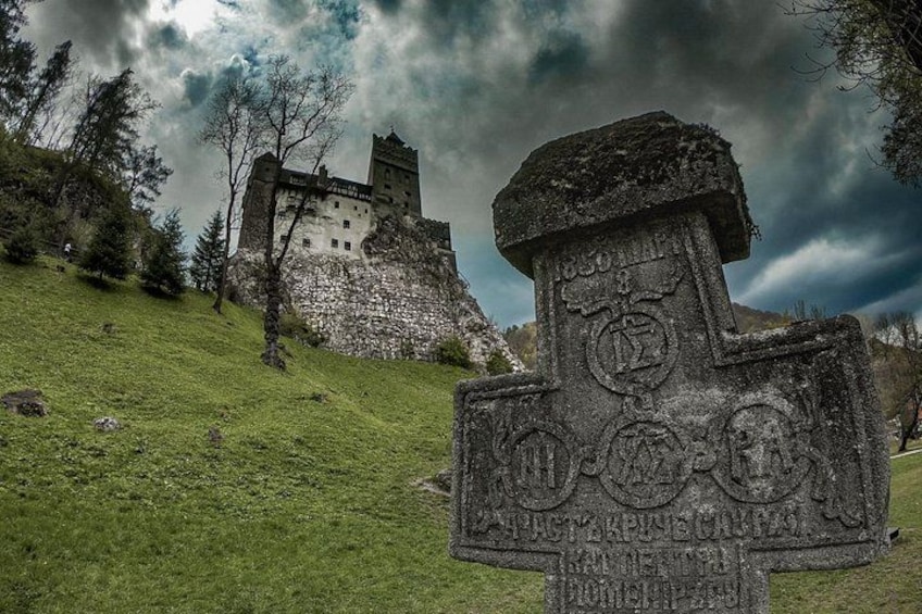 A stone monument with inscriptions, a castle in the background, and a grassy hill. 1