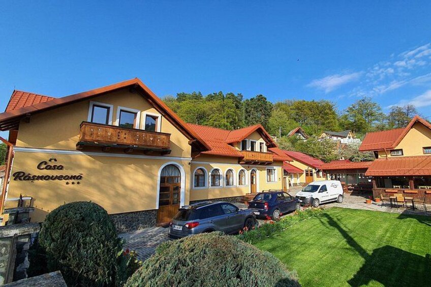 En byggnad med en skylt som visar texten ”Casa Kramovanka”, omgiven av parkerade bilar och en välskött gräsmatta. 4