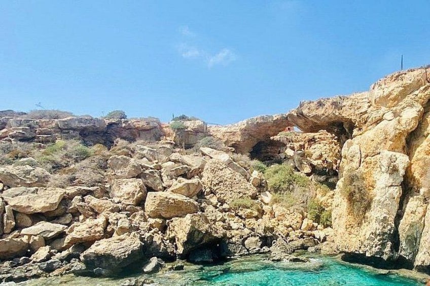 Eine felsige Küstenlandschaft mit blauem Meer, einer großen Felsformation und vereinzelter Vegetation. 5
