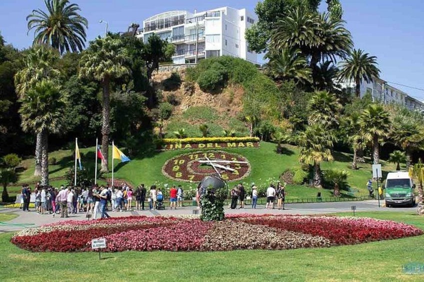 A park with a clock, palm trees, and a building in the background. 1