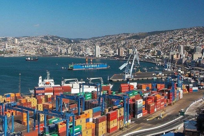 A port with shipping containers, a crane, and a cityscape in the background. 3
