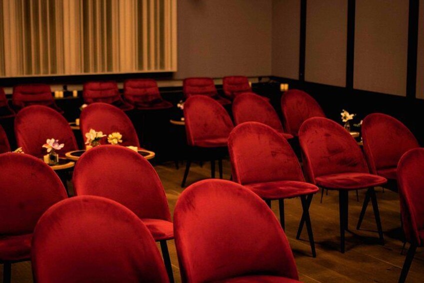 A conference room with red chairs and tables, a projector screen, and a curtain backdrop. 3