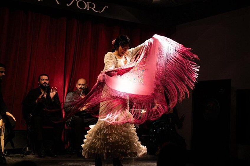 A person in a traditional dance costume performing on stage with a red curtain backdrop. 4