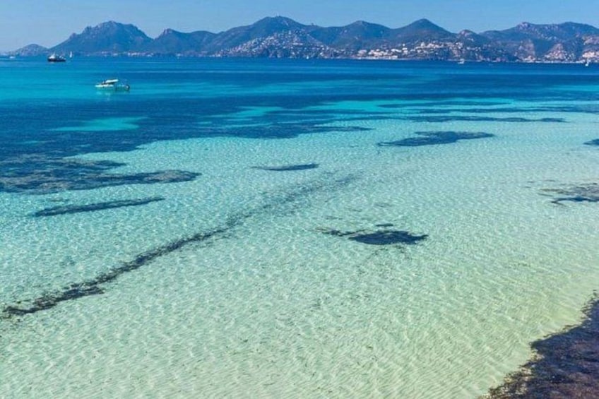 A clear turquoise sea with visible underwater rocks and a distant mountain range. 3