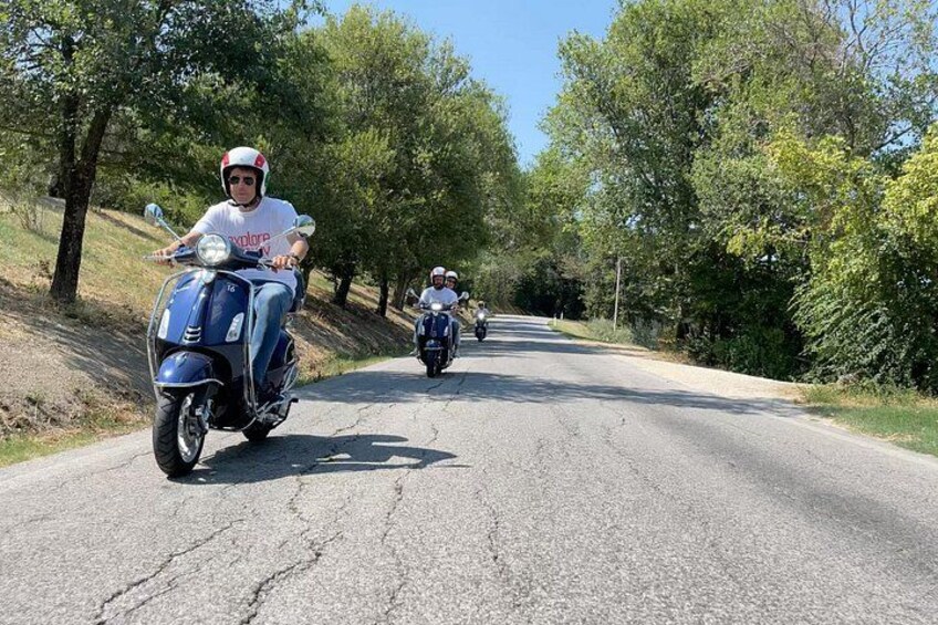 A person riding a blue scooter on a tree-lined road. 2