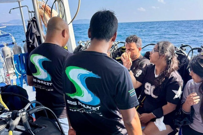 People on a boat with scuba diving equipment, wearing black t-shirts with a logo. 4