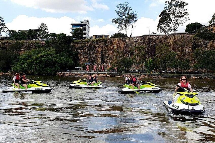 Four people riding jet skis on a body of water with a rocky cliff and trees in the background. 2